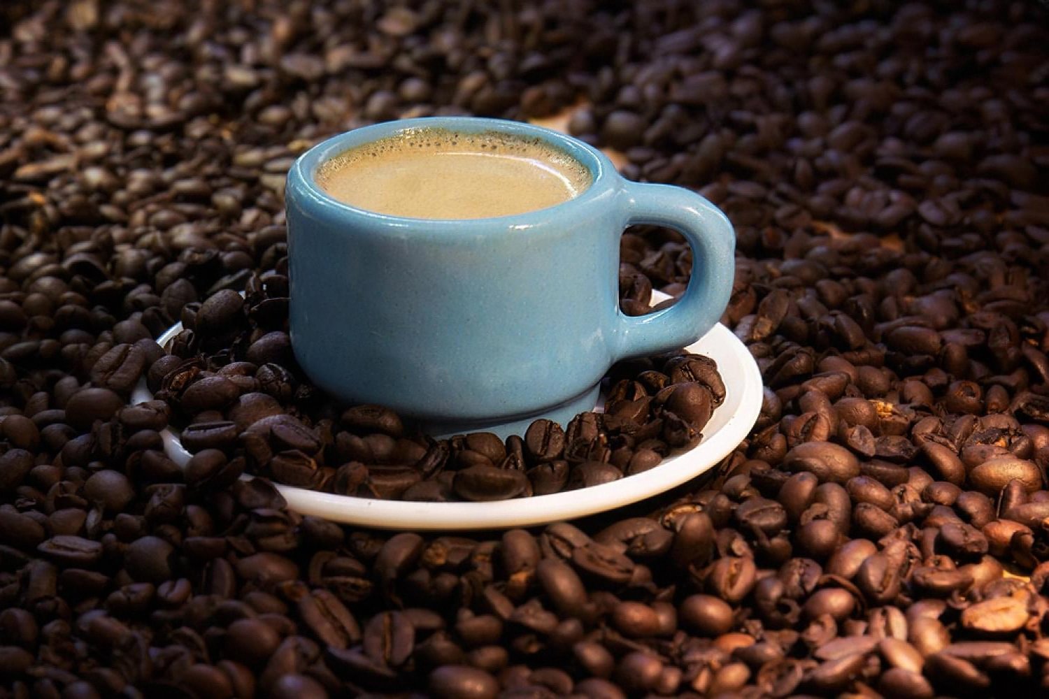 Small blue espresso cup resting on a bed of dark roasted coffee beans