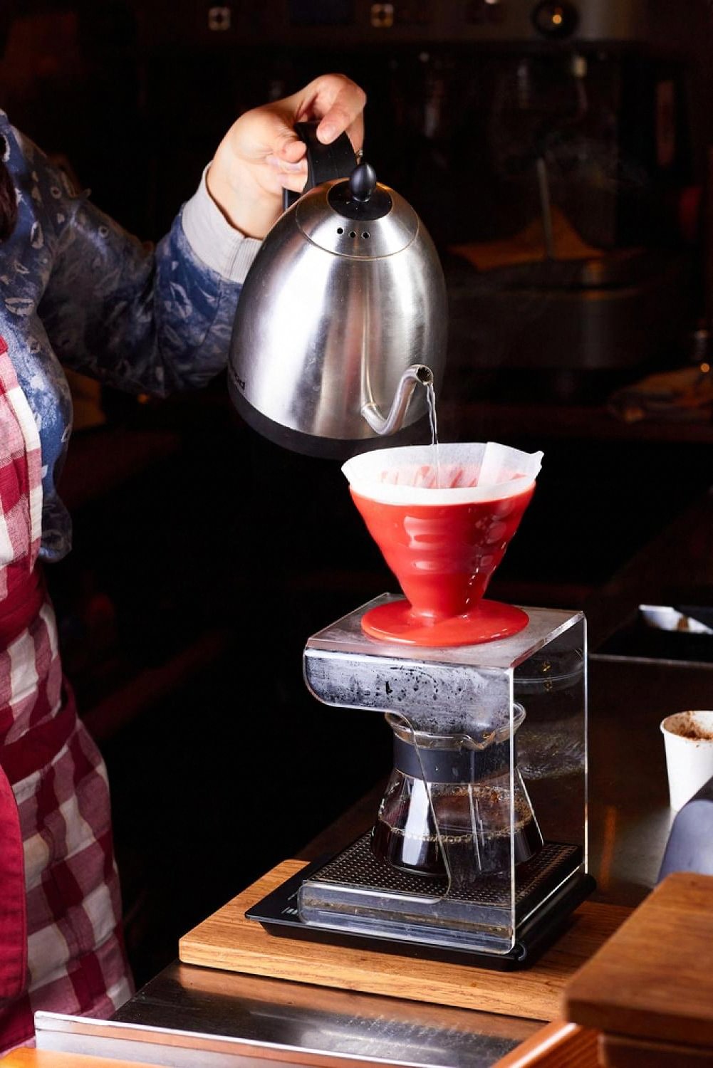 Hand pouring water from a gooseneck kettle into a red V60 dripper at a Dubai coffee bar