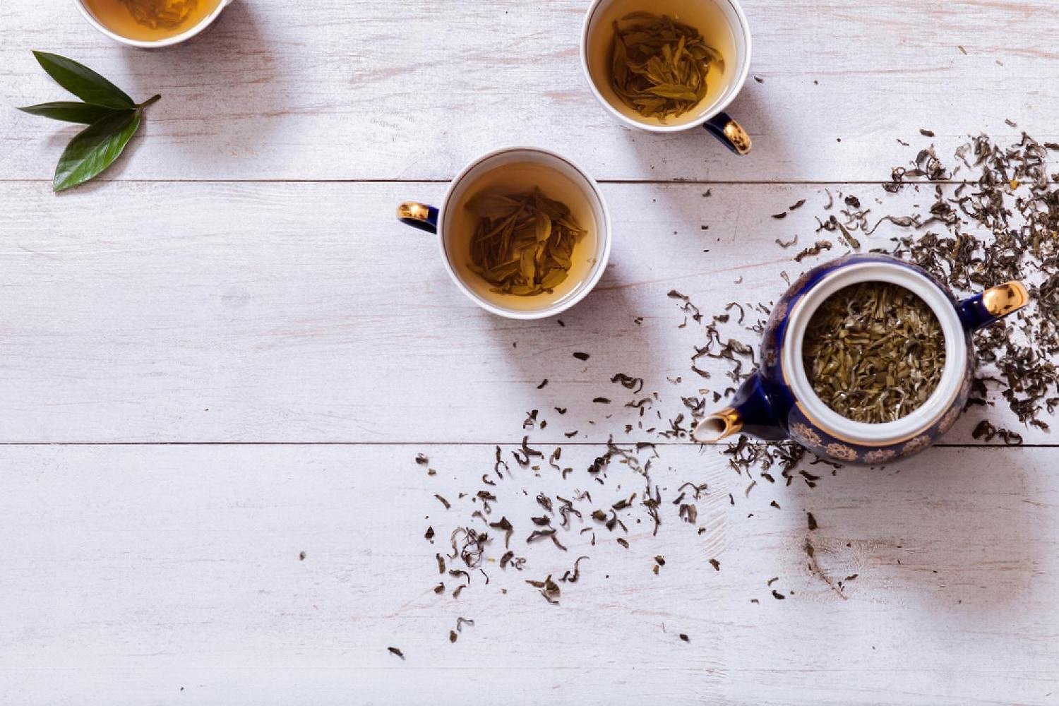 Loose-leaf oolong tea steeping in porcelain cups with a blue teapot