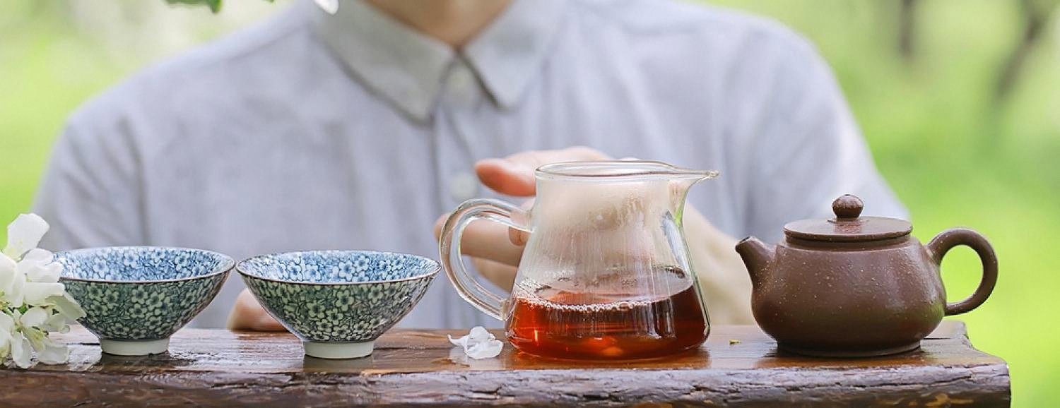 Gongfu-style oolong tea being served from a glass pitcher and clay pot