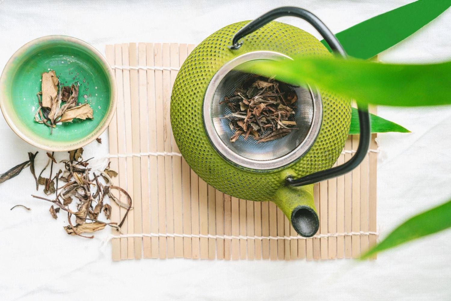 Green cast-iron teapot with dried oolong leaves on a bamboo mat